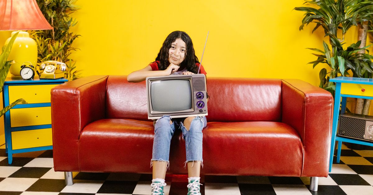Jeune femme assise sur un canapé rouge regardant une télévision à tube dans un salon coloré