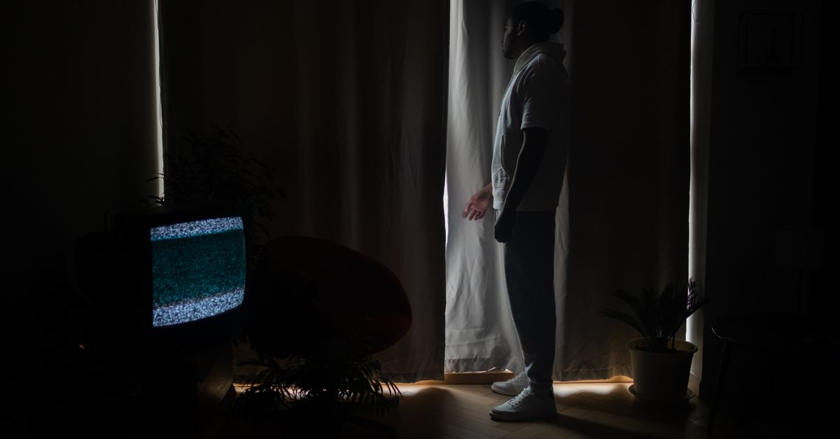 Homme debout près de rideaux, pièce sombre, écran de télévision affichant des parasites