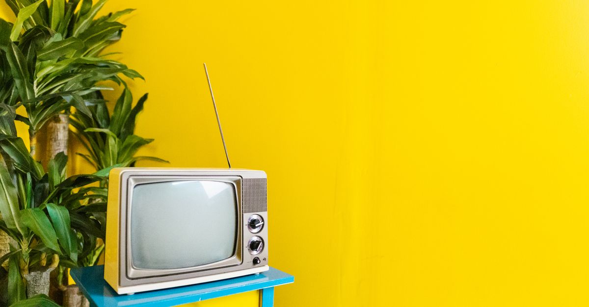 Téléviseur rétro posé sur une table bleue, plante verte à côté, mur jaune vif en arrière-plan