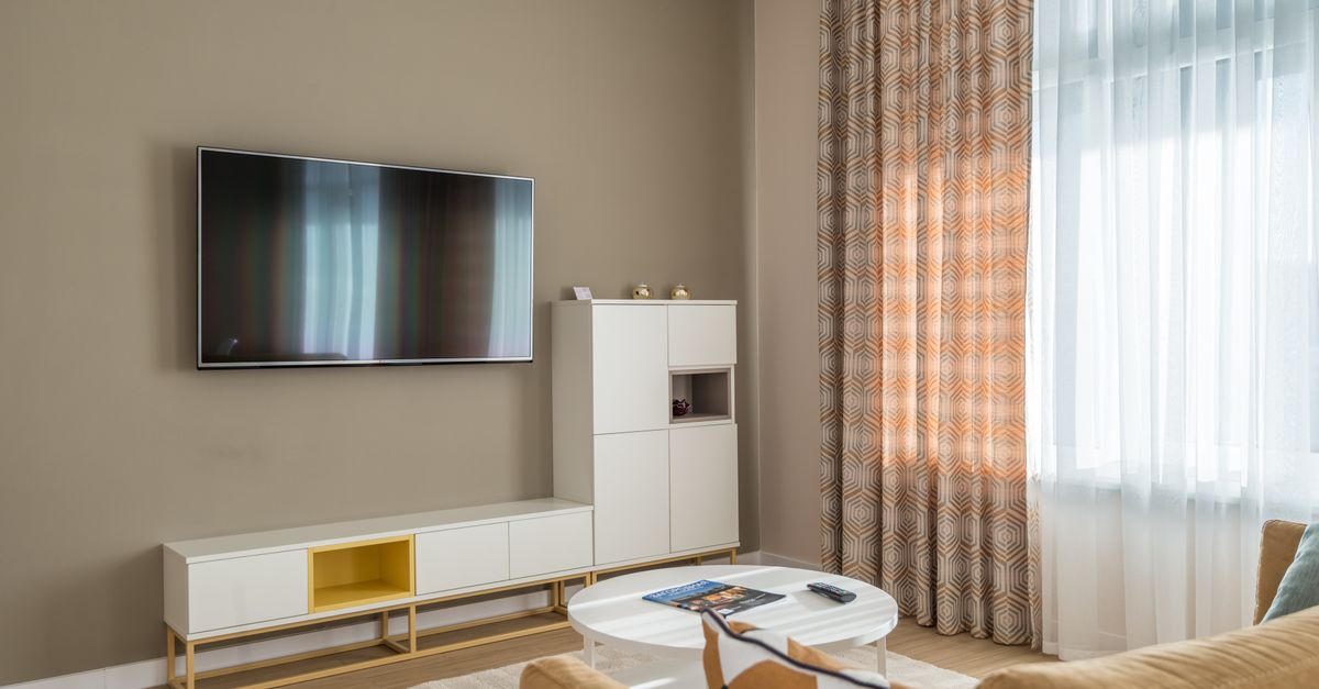 Salon moderne avec canapé clair, télévision à écran plat allumée et décoration épurée autour