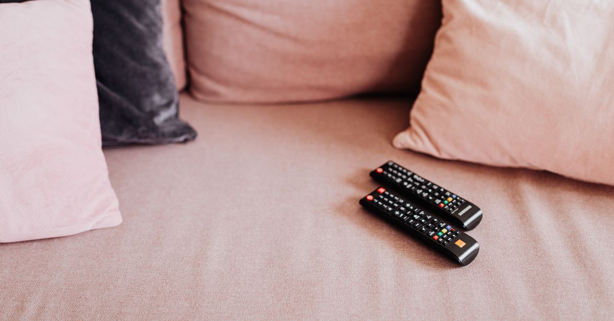 Deux télécommandes posées sur un canapé rose entouré de coussins douillets