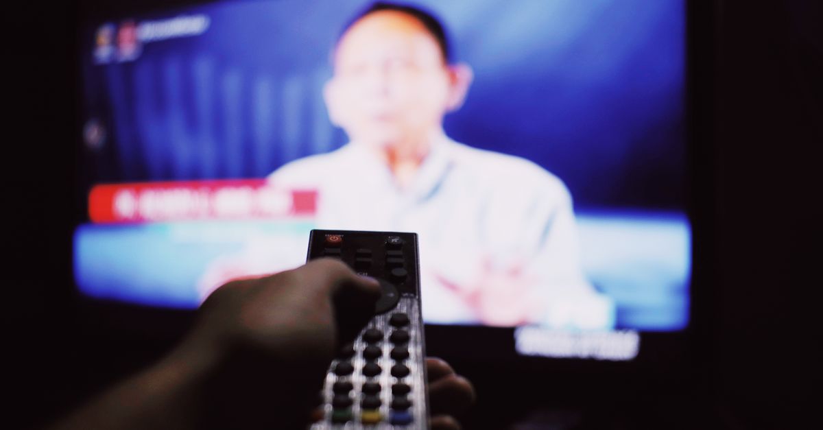 Main anonyme utilisant une télécommande devant une télévision allumée dans un salon tamisé