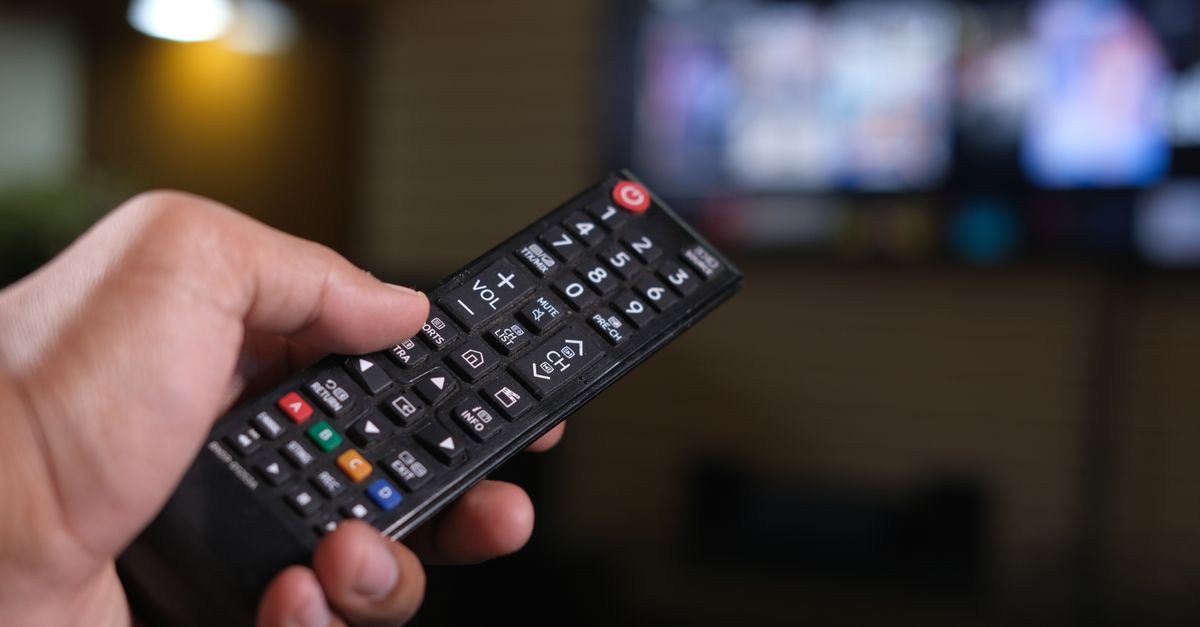 Personne tenant une télécommande devant un écran de télévision flou en arrière-plan