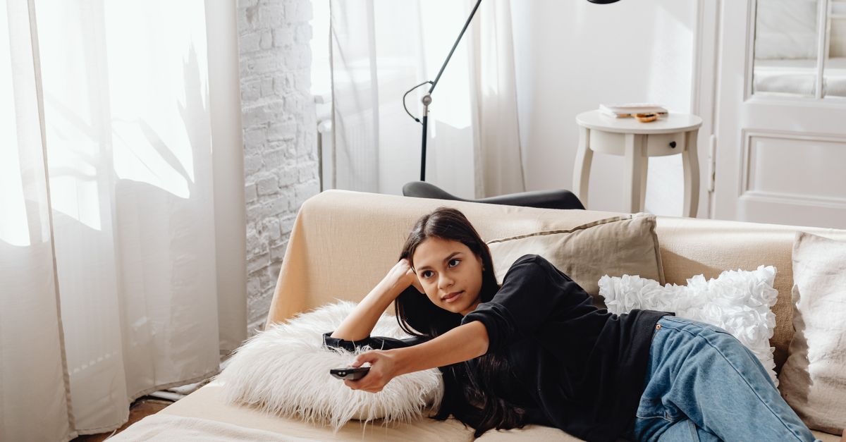 Jeune femme détendue sur un canapé, télécommande à la main, profitant d’un moment de détente devant la télévision