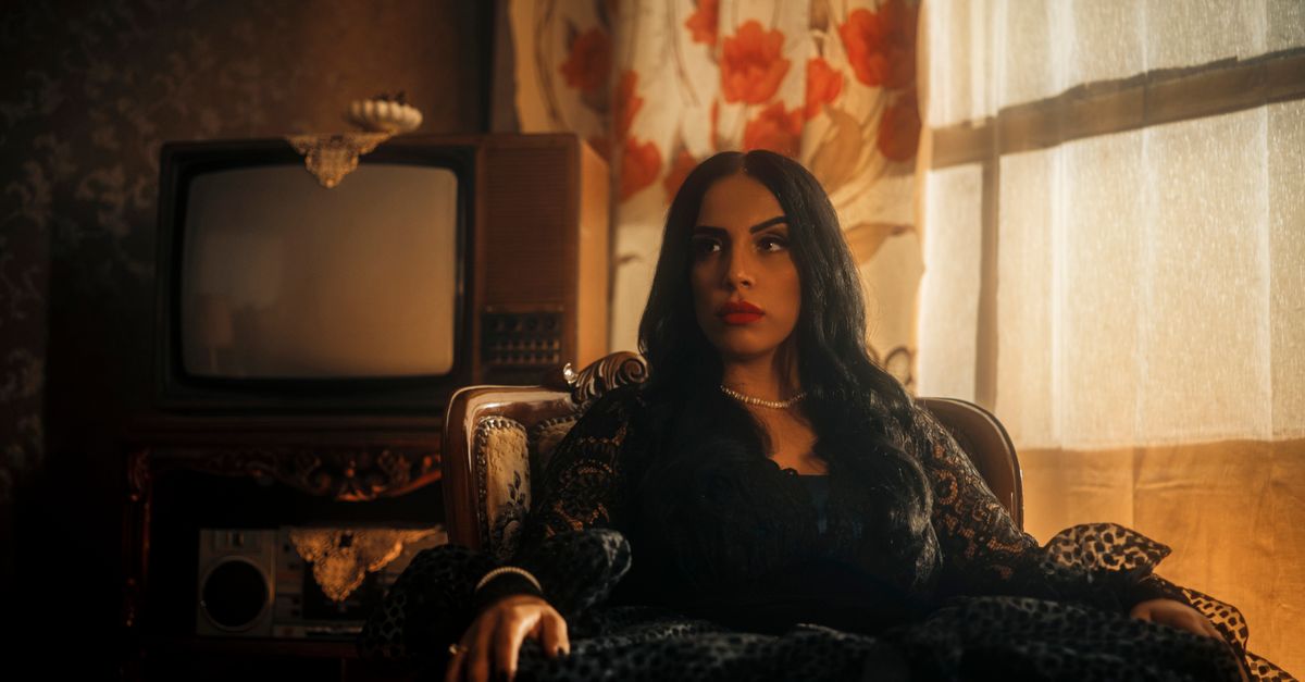 Femme en robe noire à côté d’un téléviseur ancien dans un salon rétro