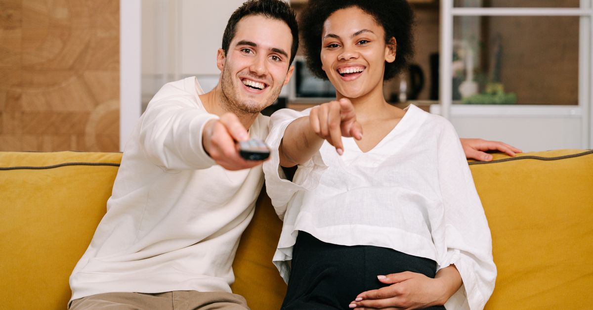 Un couple souriant assis sur un canapé jaune regarde un film ensemble à la télévision