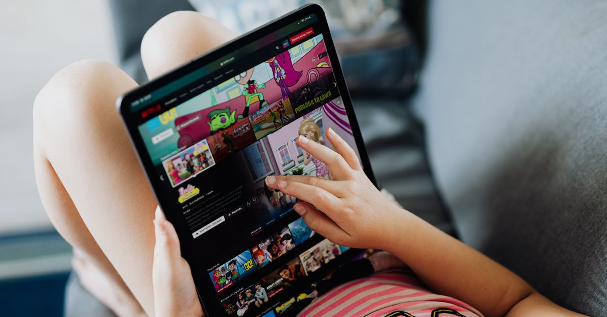 Enfant détendu sur un canapé utilisant une tablette pour regarder des dessins animés en streaming.