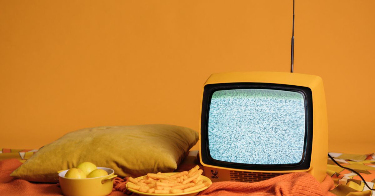 Téléviseur jaune rétro diffusant de la neige, posé sur un coussin entre frites et pommes