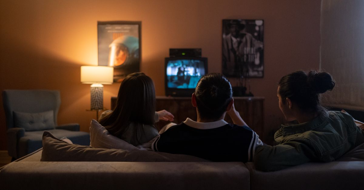 Trois amis assis sur un canapé regardant un film ensemble dans un salon douillet