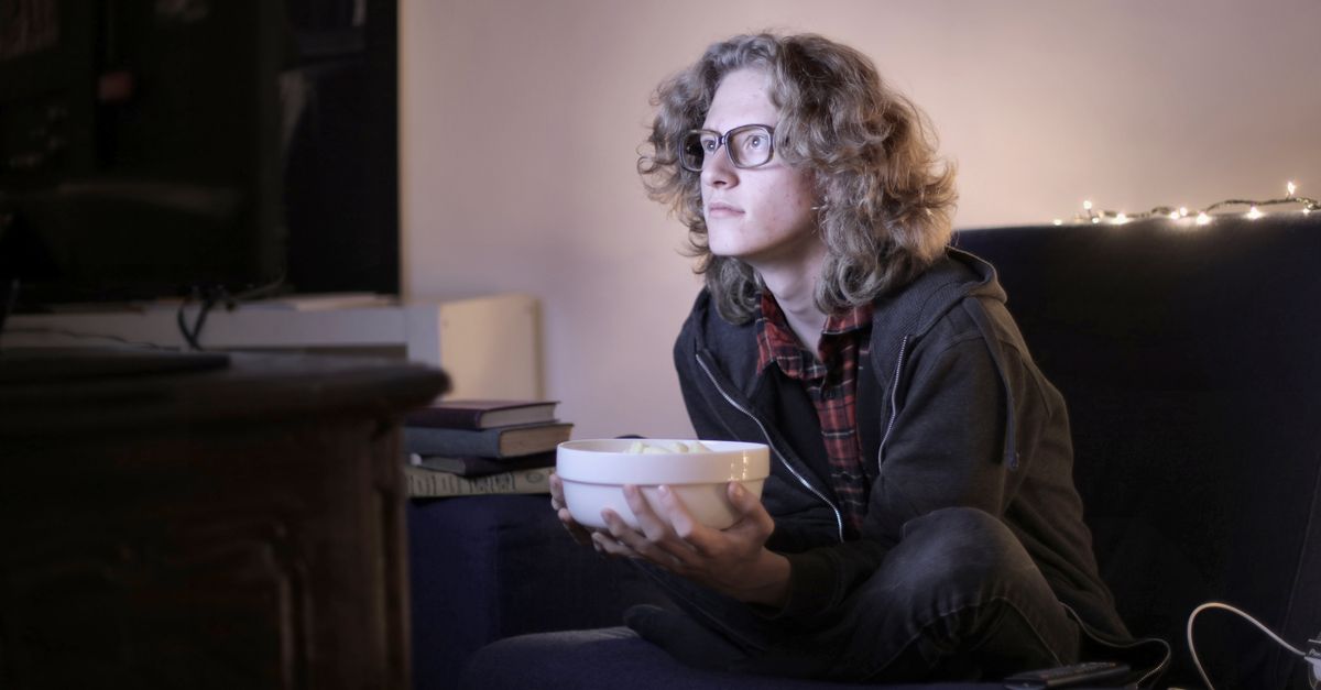 Jeune homme concentré mangeant du pop-corn devant la télévision dans un salon confortable