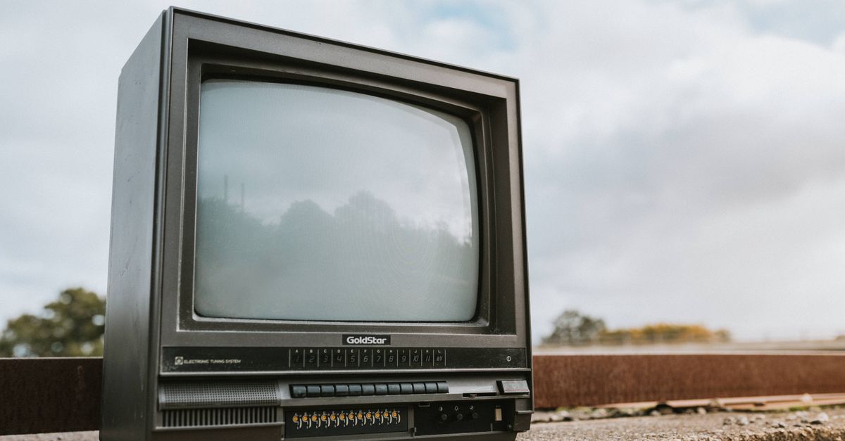 Téléviseur ancien posé sur une rambarde en béton sous un ciel nuageux en ville