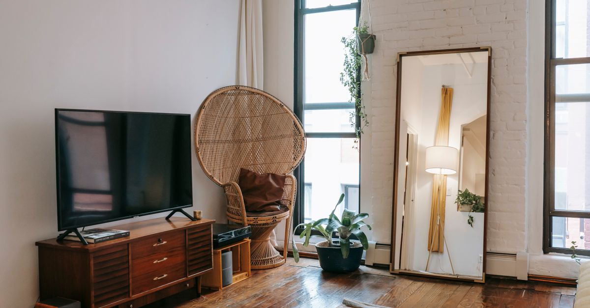 Salon chaleureux avec fauteuil en osier et télévision posée sur une commode blanche