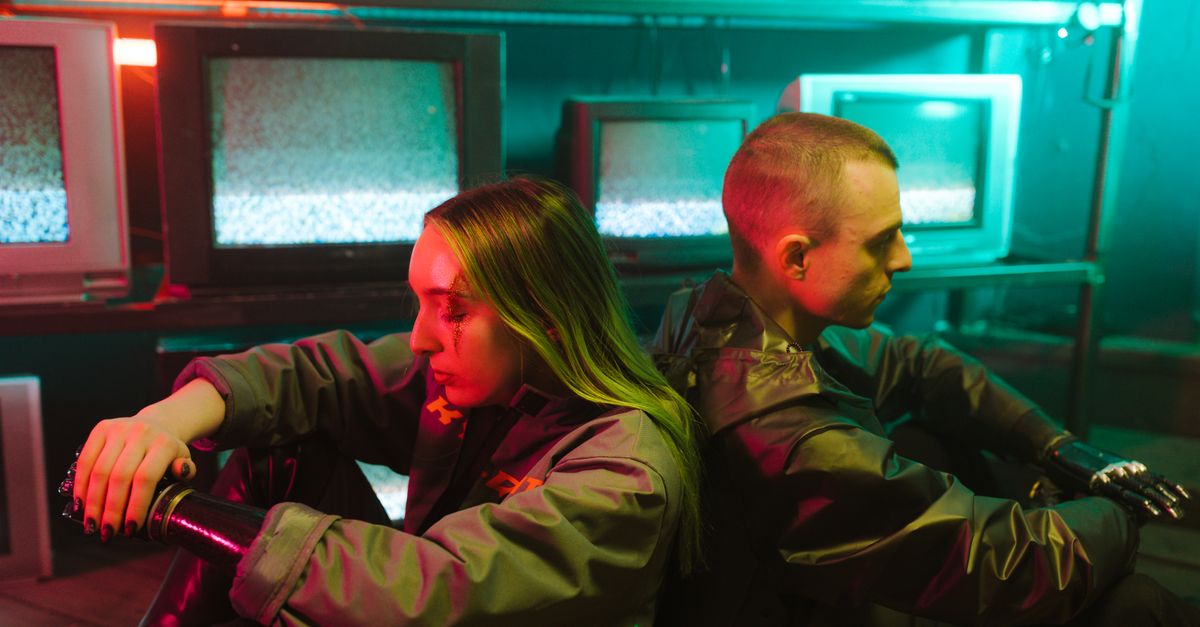 Deux personnes dans un décor futuriste entourées de nombreux téléviseurs lumineux