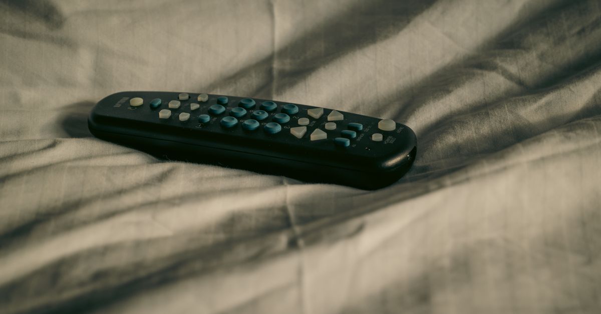 Télécommande posée sur des draps froissés, ambiance détendue dans une chambre cosy.