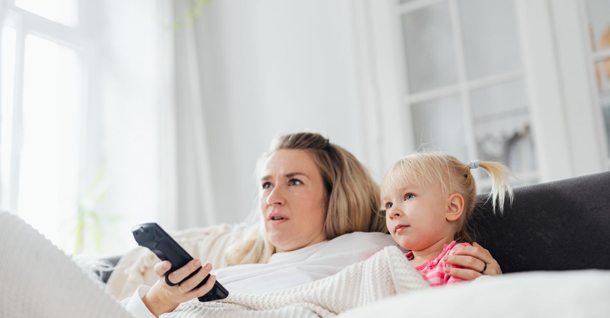 Mère et fille détendues sur un canapé, tenant une télécommande dans un salon lumineux