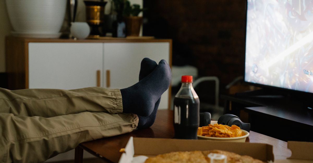 Personne en chaussettes dégustant des chips et du cola devant la télévision dans un salon