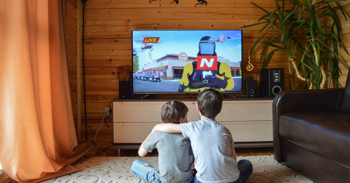 Deux enfants enlacés assis par terre regardant un dessin animé sur un grand écran à la maison