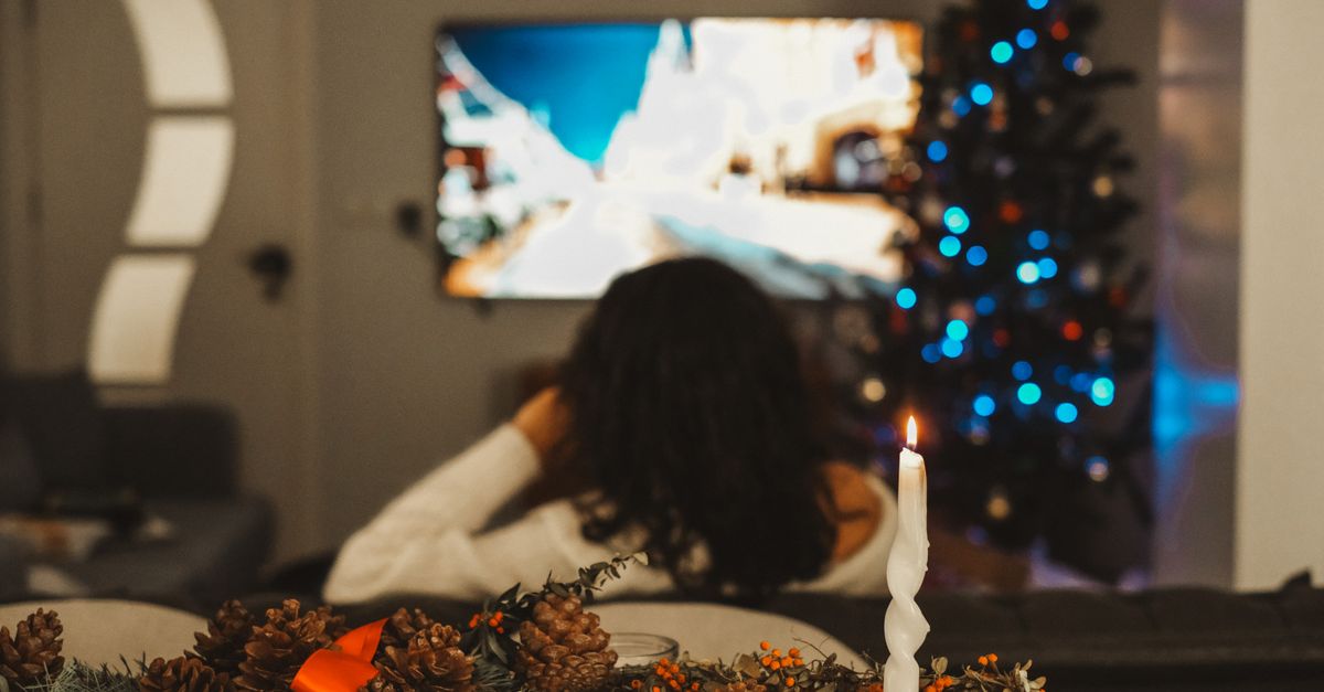 Femme assise sur un canapé regardant la télévision près du sapin de Noël allumé