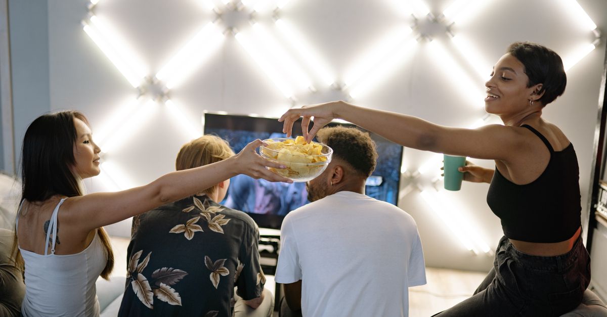 Des amis assis sur un canapé regardent la télévision tout en partageant des snacks