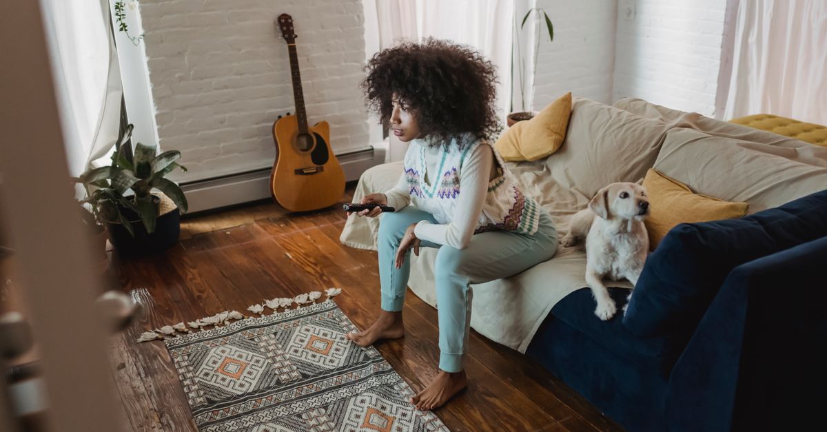 Femme assise pieds nus sur le canapé avec son chien regardant la télévision dans un intérieur chaleureux