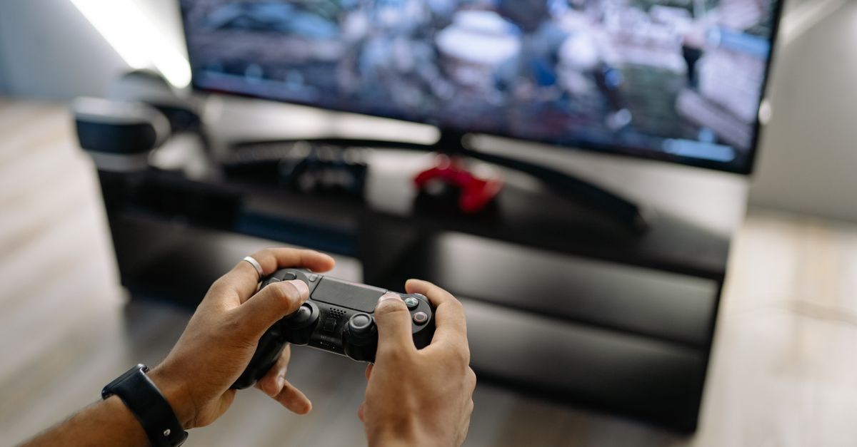 Mains tenant une manette de jeu devant un écran de télévision allumé dans un salon