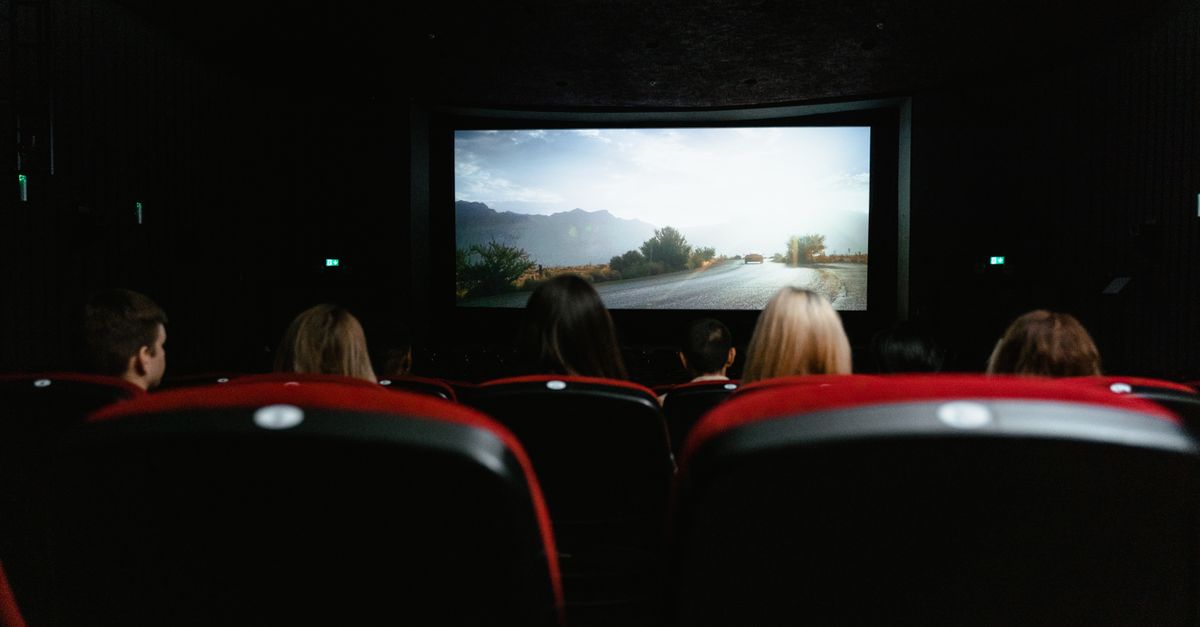 Vue arrière sur des spectateurs assis dans une salle de cinéma devant un grand écran lumineux.