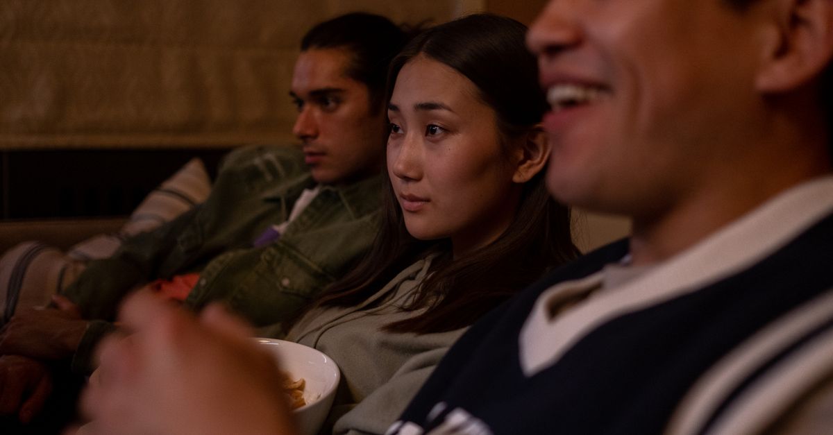 Groupe d’amis assis sur un canapé partageant des encas tout en regardant un film.
