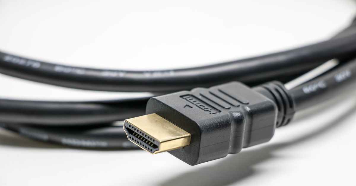 Câble HDMI noir avec connecteurs dorés posé sur une surface blanche, bien éclairé.