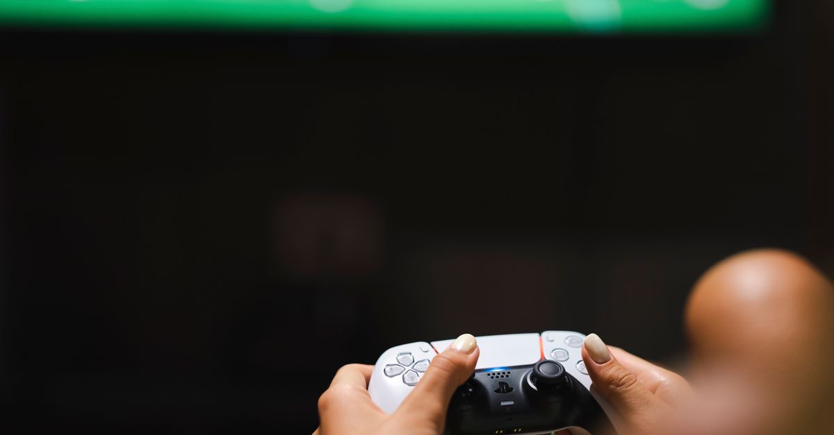 Mains tenant une manette de jeu vidéo moderne devant un écran en train de jouer