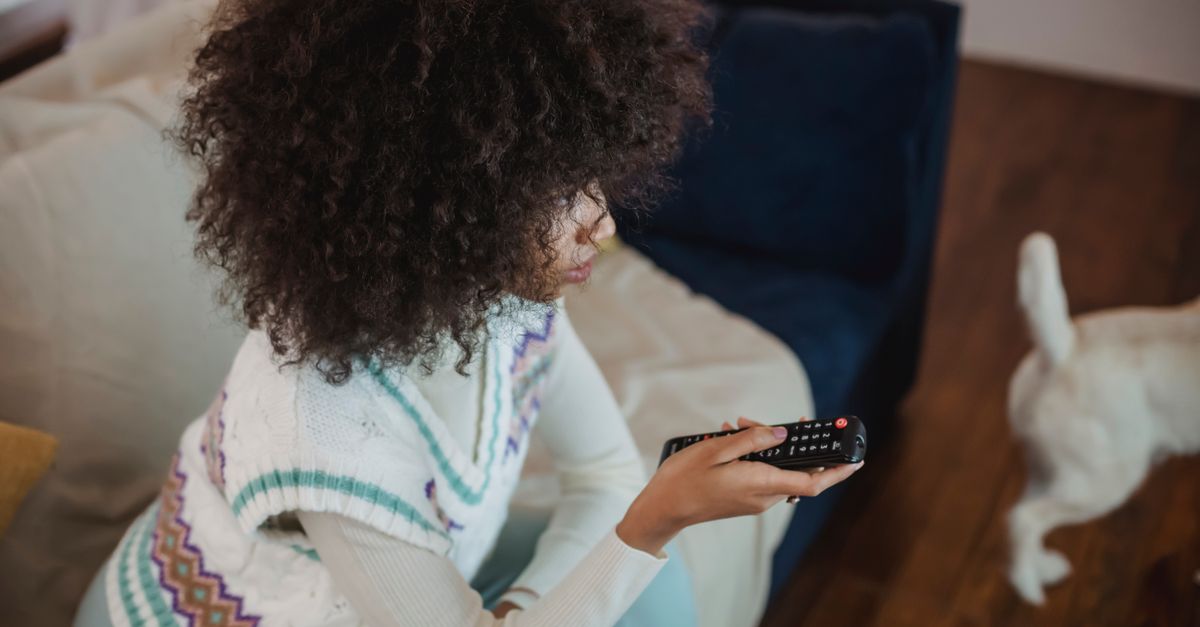 Jeune femme assise sur un canapé avec une télécommande, regardant la télévision avec son chien
