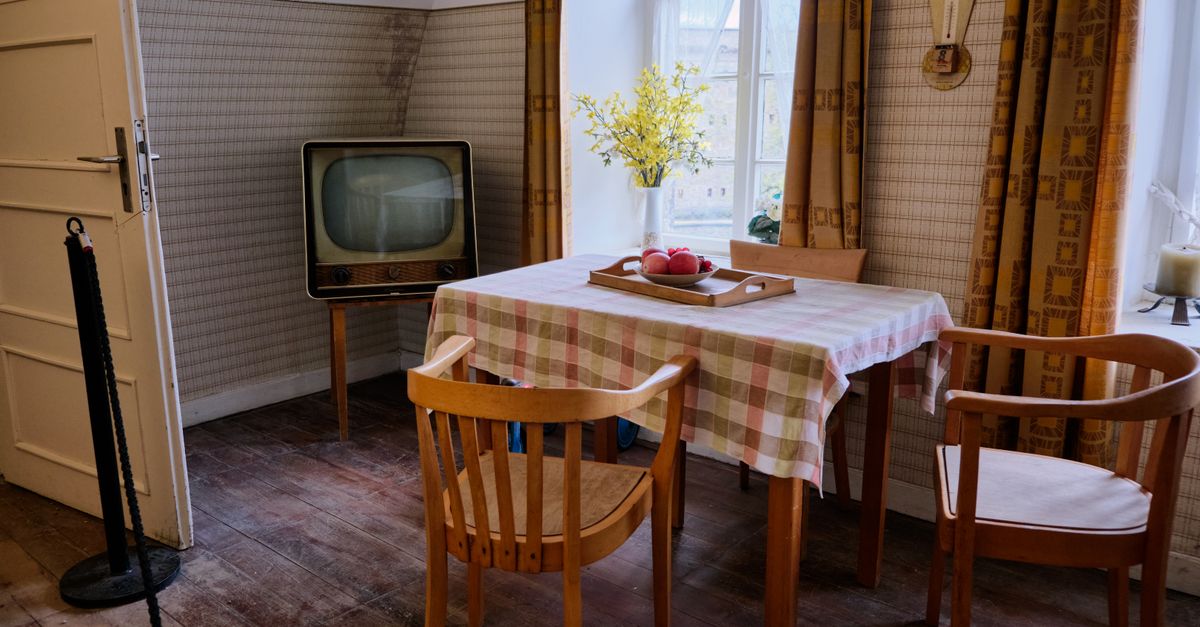 Salle à manger rétro avec un vieux téléviseur, des chaises en bois et une nappe à carreaux