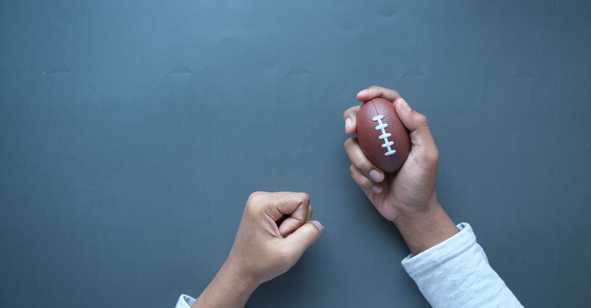 Mains tenant un petit ballon de football posé sur une surface bleue unie