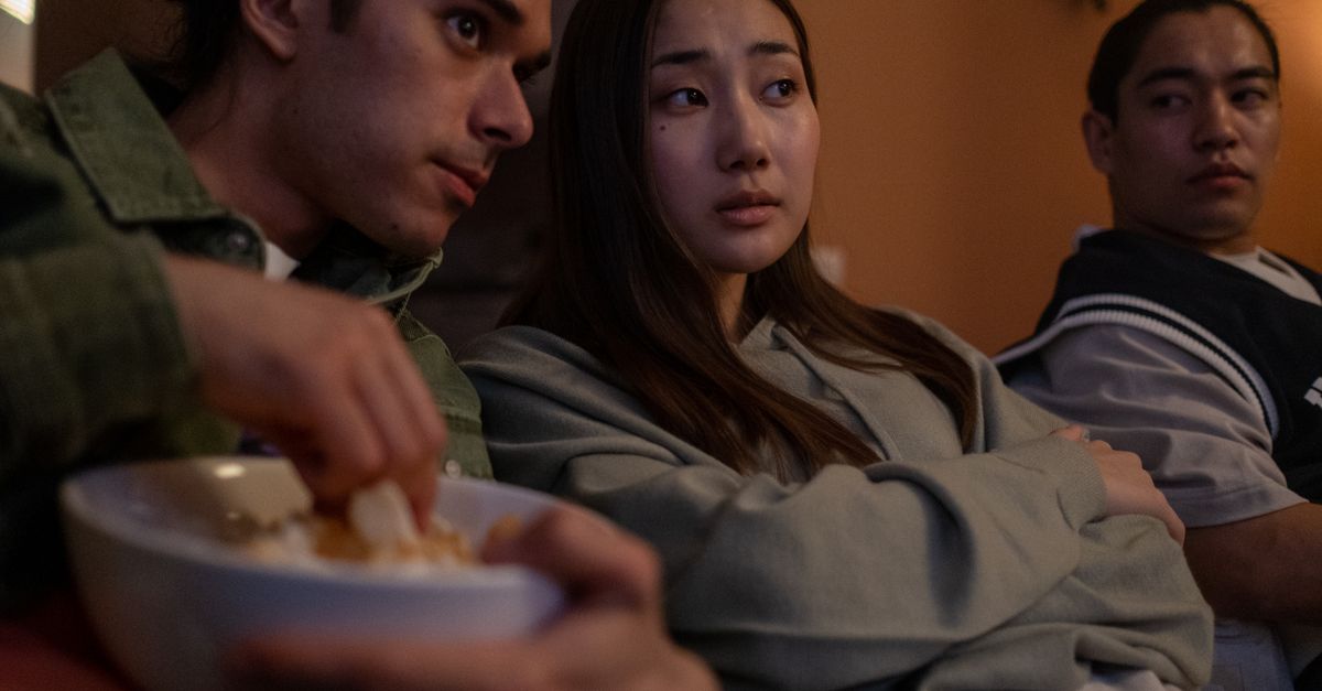 Trois adolescents assis regardant la télévision et partageant des snacks dans une ambiance conviviale