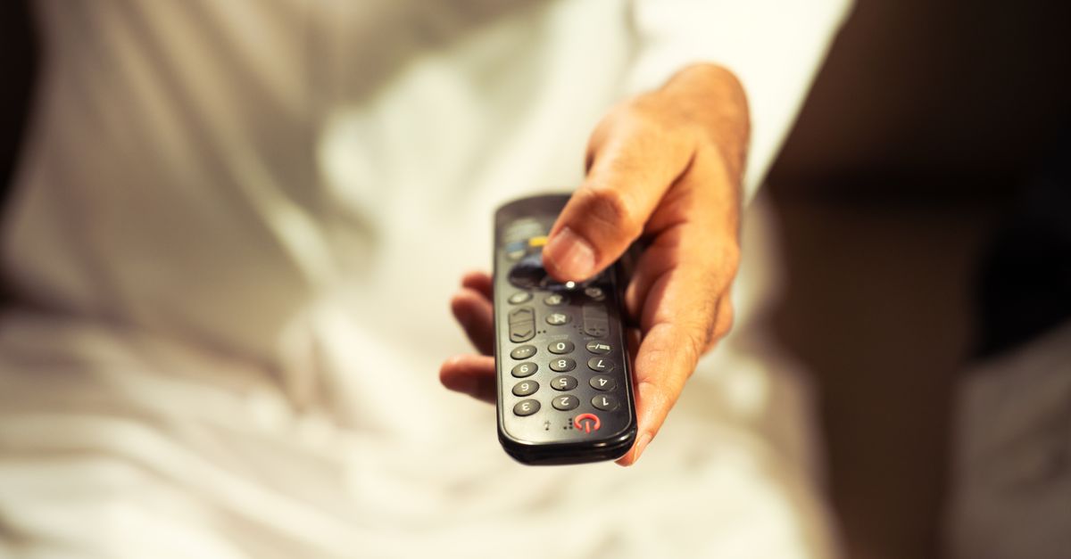 Main tenant une télécommande devant un téléviseur, ambiance détente au salon