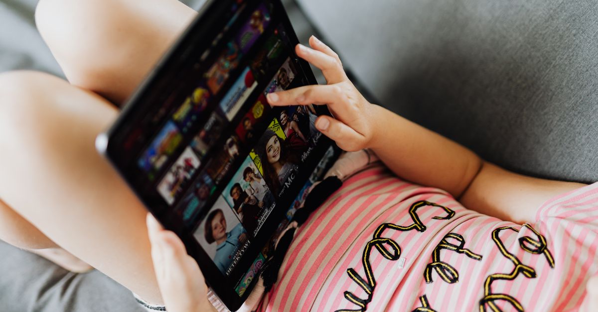 Jeune fille allongée sur un tapis utilisant une tablette pour regarder des vidéos
