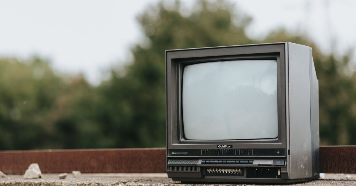 Petite télévision noire rétro posée sur une rambarde en pierre devant des arbres en ville