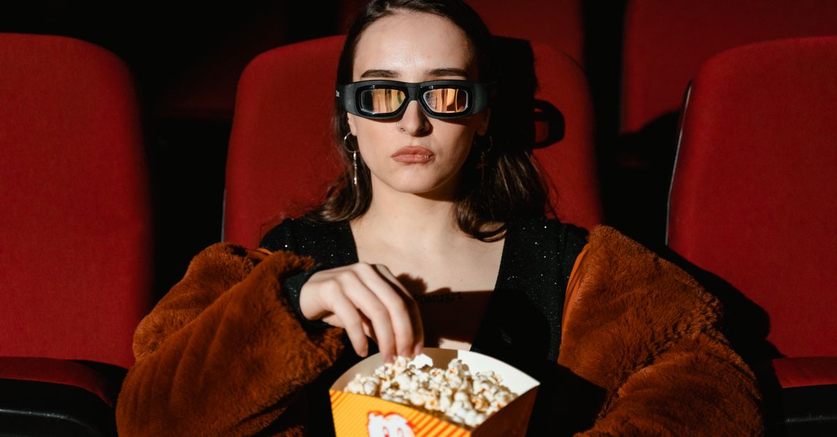 Femme en manteau de fourrure mangeant du popcorn devant un film en 3D au cinéma
