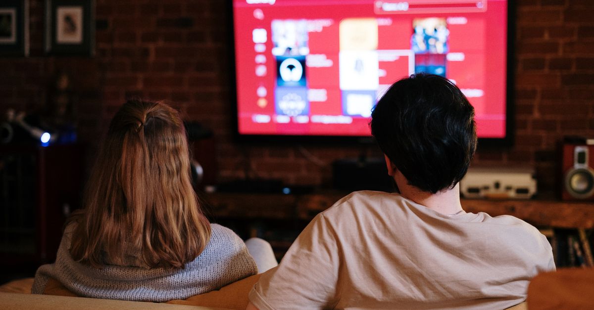 Un couple regarde une série sur une grande télévision dans un salon chaleureux aux murs en briques
