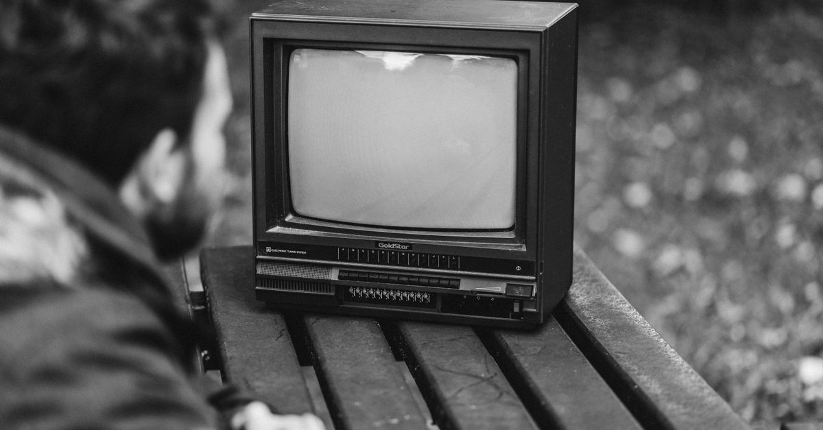 Homme assis à une table en bois regardant une télévision ancienne en plein air