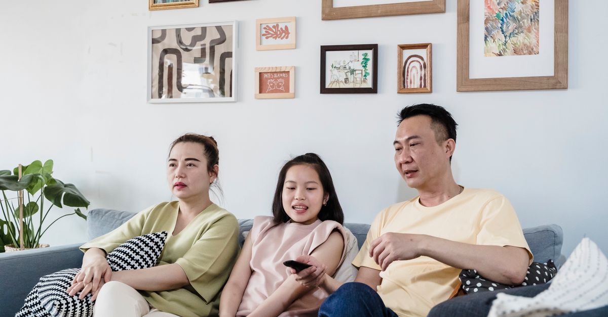 Famille de trois personnes détendue sur un canapé regardant un programme télévisé ensemble