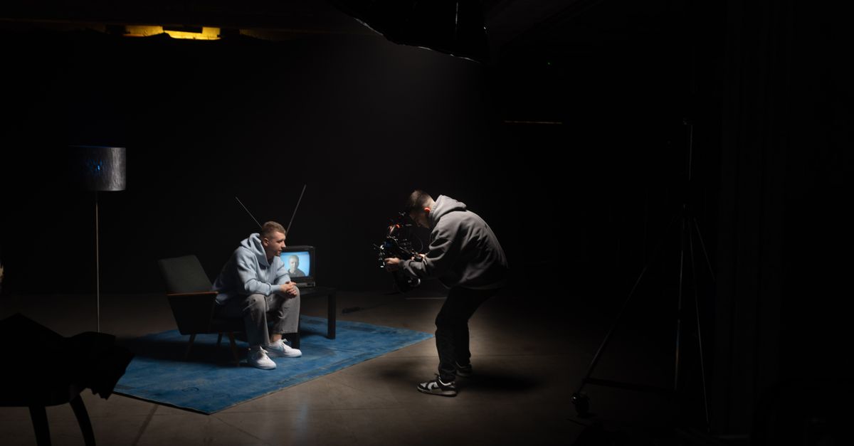 Tournage en intérieur avec un cadreur filmant un acteur assis sous des lumières de studio.