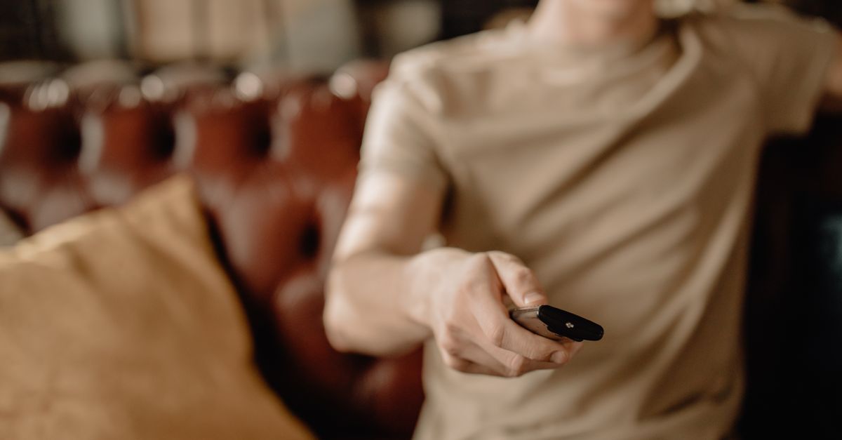 Personne assise sur un canapé en cuir, télécommande à la main dans une ambiance détendue.