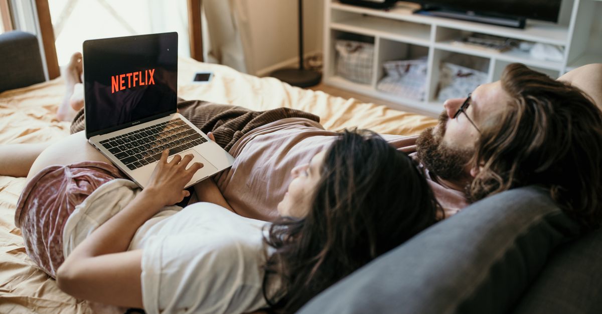 Couple détendu allongé sur un lit, regardant un film sur ordinateur portable.