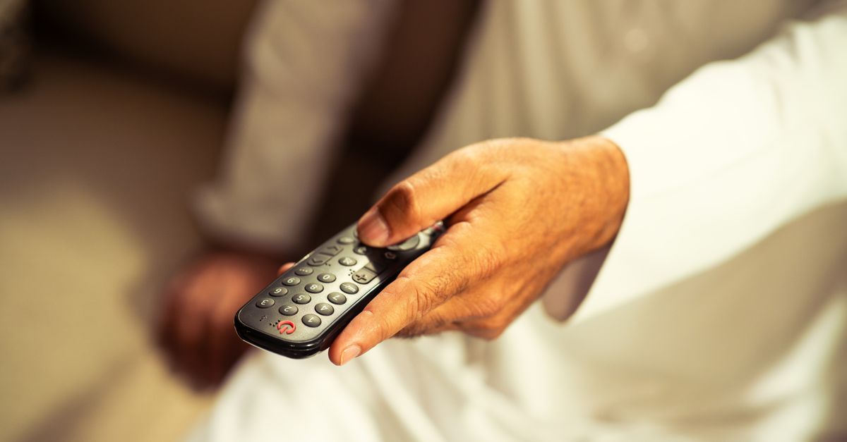 Main adulte tenant une télécommande de télévision en gros plan dans un salon lumineux