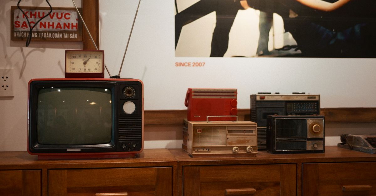Plusieurs téléviseurs et radios anciens posés sur un meuble en bois dans une pièce rétro