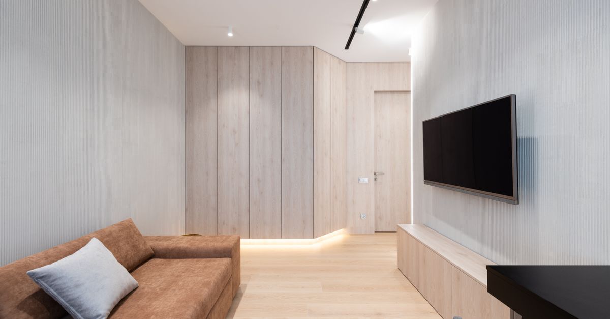 Salon moderne avec canapé, coussins et télévision murale près d’une table basse