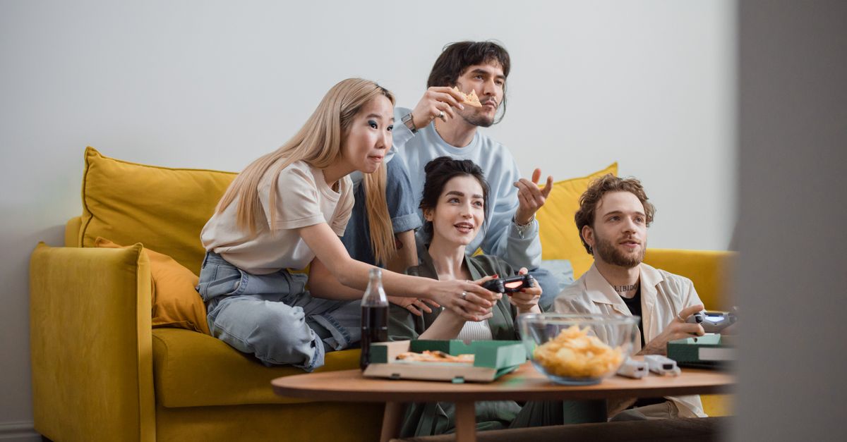 Groupe d’amis jouant sur un canapé jaune avec des snacks dans une ambiance détendue
