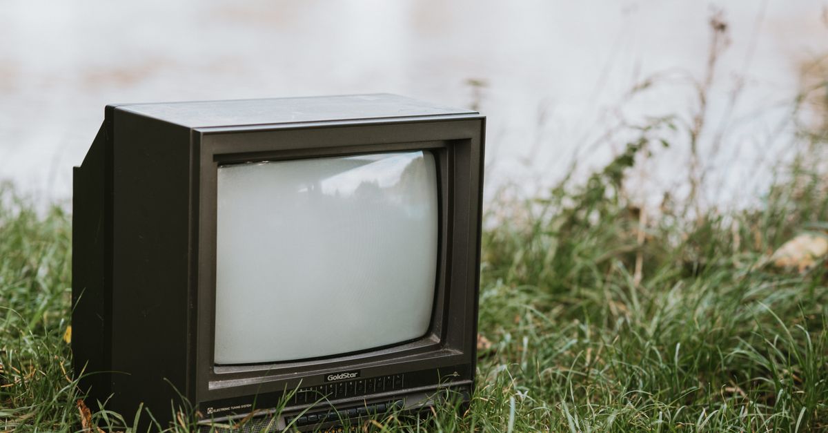 Petit téléviseur ancien posé sur l’herbe près d’un plan d’eau paisible