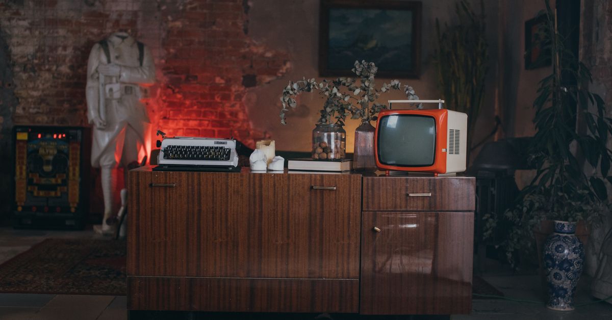 Salon rétro avec vieille télévision et machine à écrire posées sur un meuble ancien.