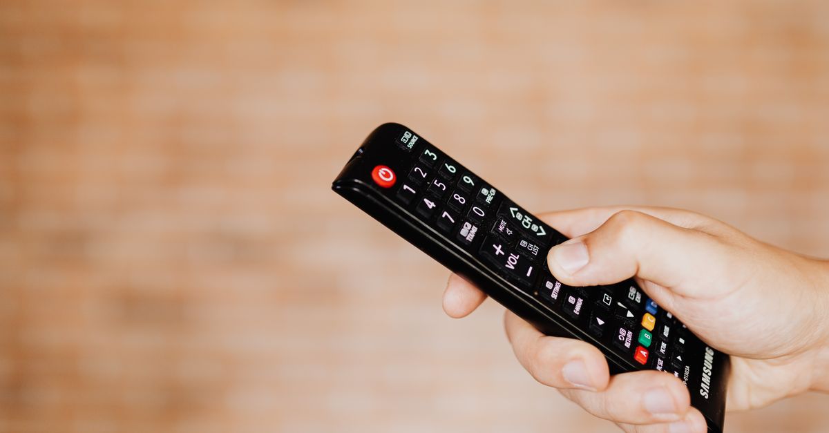 Main tenant une télécommande devant un fond flou, prête à changer de chaîne.